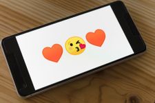 A smartphone with a kiss face emoji that has orange heart emojis either side