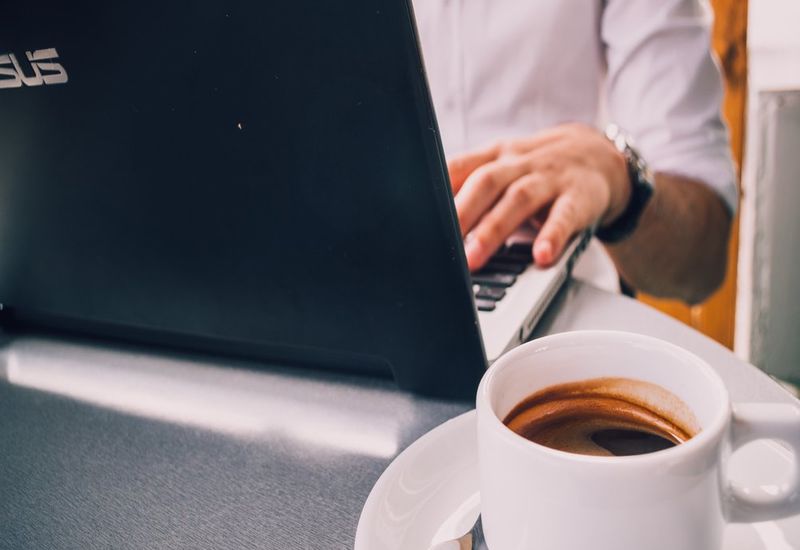 Person in a white shirt sat at their laptop with a half-full cup of coffee