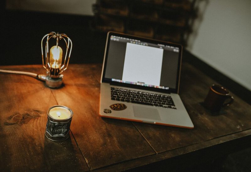 Laptop on a dark wood desk with a lamp and a coffee cup